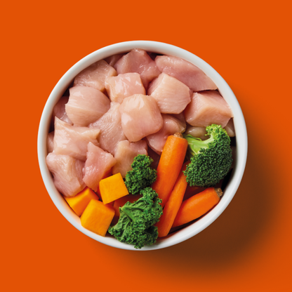 Raw British chicken cubes, carrots, broccoli, sweet potato on orange background. Product: Raw Chicken 1kg.