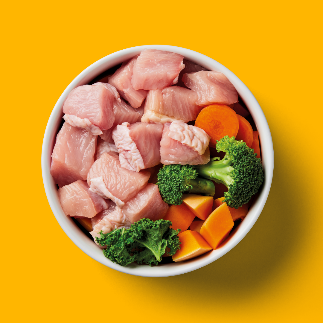 Raw Turkey 1.4kg with fresh broccoli, carrots, and kale on a bright yellow background.