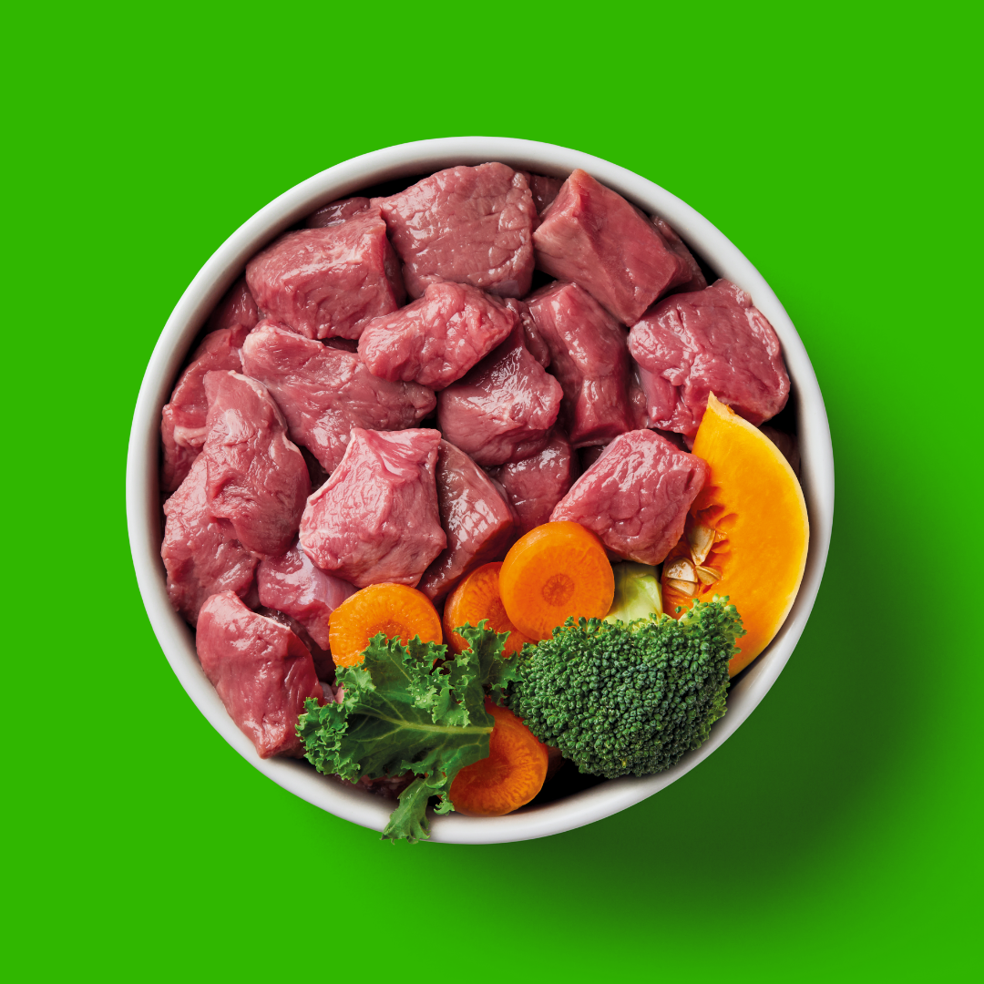 Raw Lamb 1.4kg with superfoods broccoli, carrots, and kale on a vibrant green background.