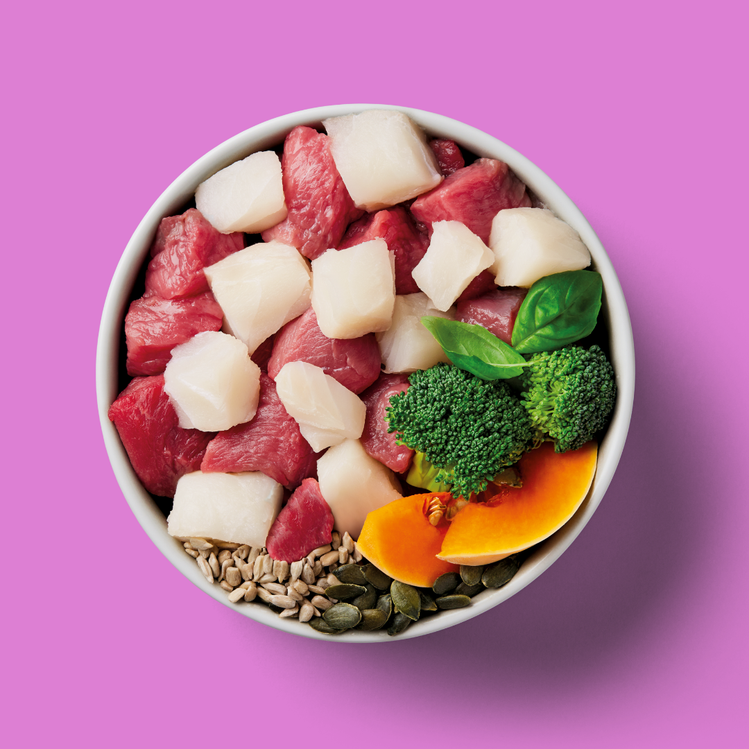 Bowl of Liver Support 500g with raw meat, white fish, veggies, seeds, and basil on a pink background.