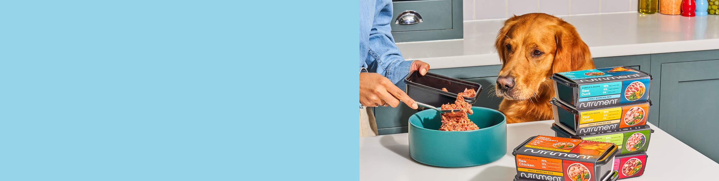 Person preparing dog food in a bowl next to a dog, with stacked Nutriment pet food containers on the counter.