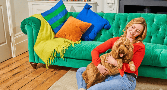 Woman sitting in front of a velvet green sofa with a golden cockapoo on her lap.