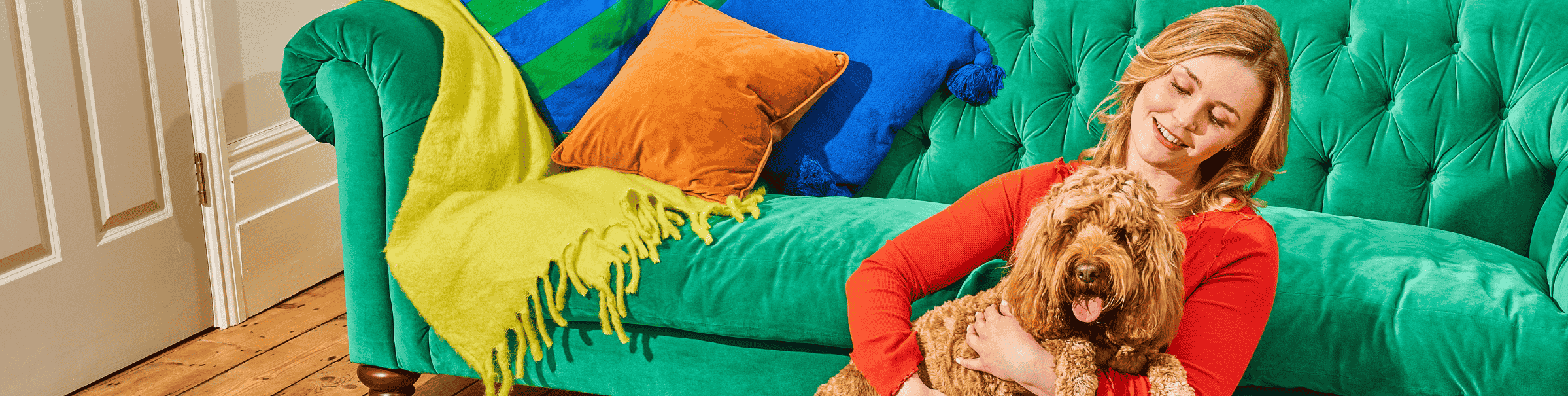 Woman smiling and holding a fluffy brown dog on a vibrant green sofa with colorful cushions.